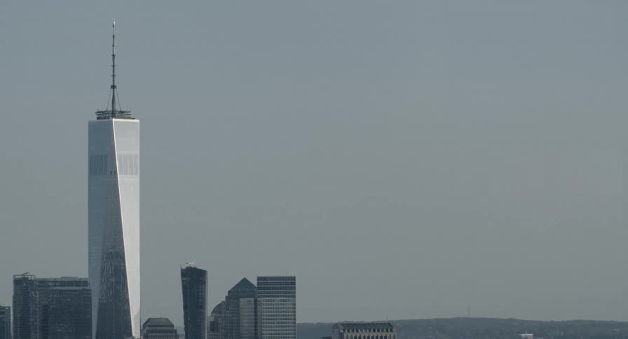Static long shot of One World Trade Center standing tall against a hazy New York City sky