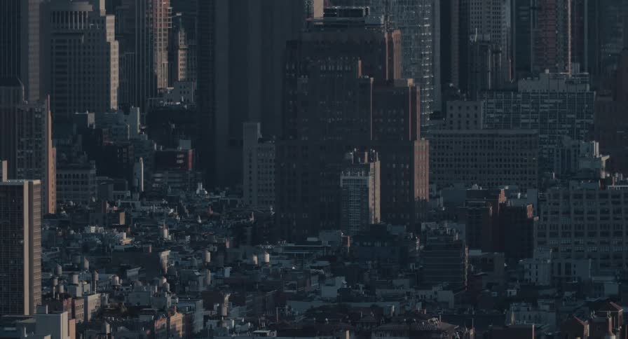 A static view of a dense New York City cityscape with buildings covered in shadow during the early morning