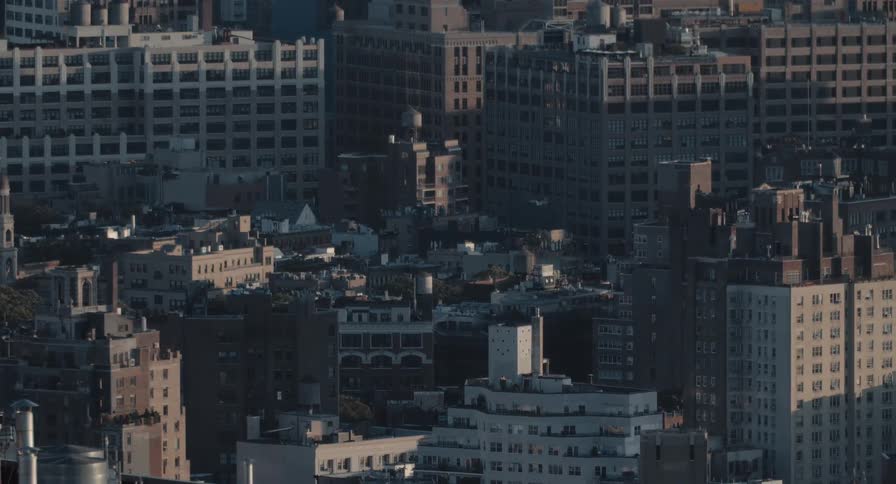 Time-lapse from a high angle captures the shifting light and shadows across the dense buildings and rooftops of an urban city