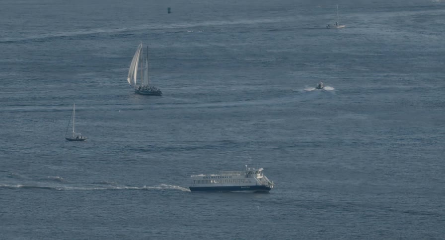 An aerial view captures a ferry, sailboats, and a motorboat cruising on the open water