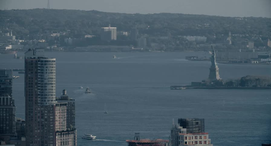 A high-angle, hazy view of boats and ferries sailing on the Hudson River with the Statue of Liberty visible in the distance