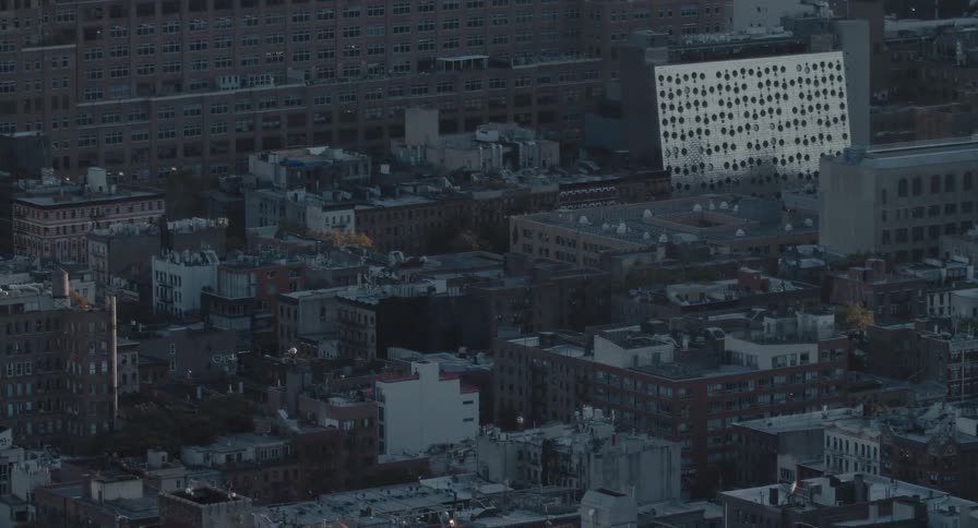 A high-angle, static shot captures a quiet city neighborhood with a mix of modern and classic brick buildings at dawn