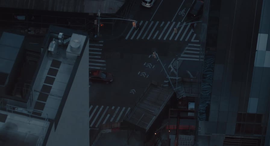 A moody high-angle view of a quiet city intersection at dusk as cars and pedestrians cross the street