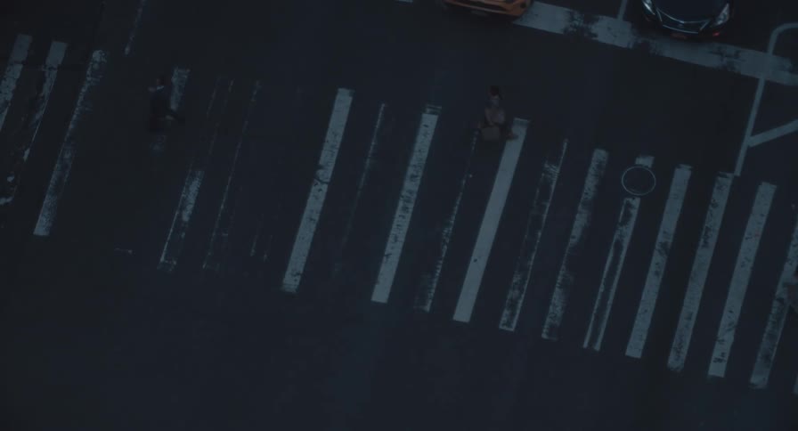 A dark, moody high-angle top-down shot of various pedestrians and cyclists crossing a weathered city crosswalk at night