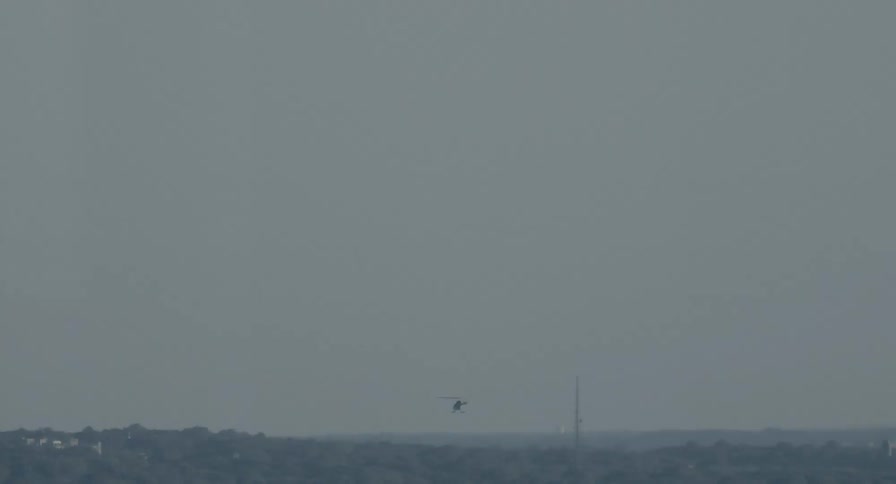 A lone helicopter flies slowly across the distant horizon under a hazy grey sky