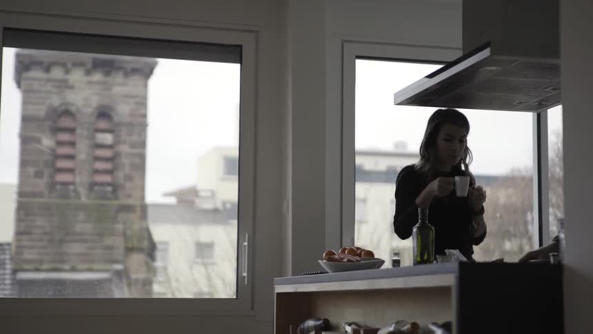 A woman is drinking from a mug in the kitchen