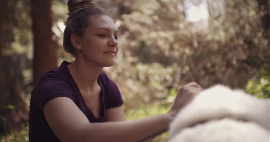 Woman smiles as she pets a dog outside in the woods
