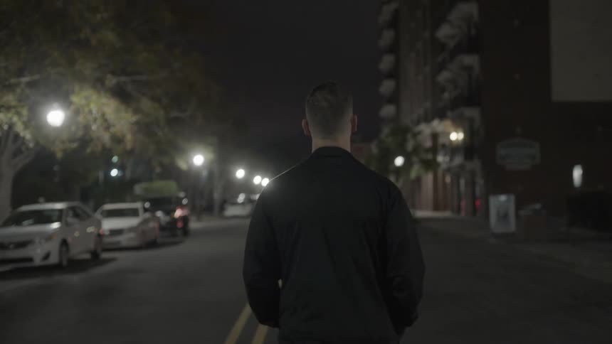 A man walks down the middle of an urban street at night