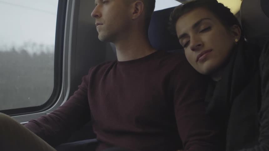 Couple riding on a train as the woman rests her head on the man's shoulder with her eyes closed