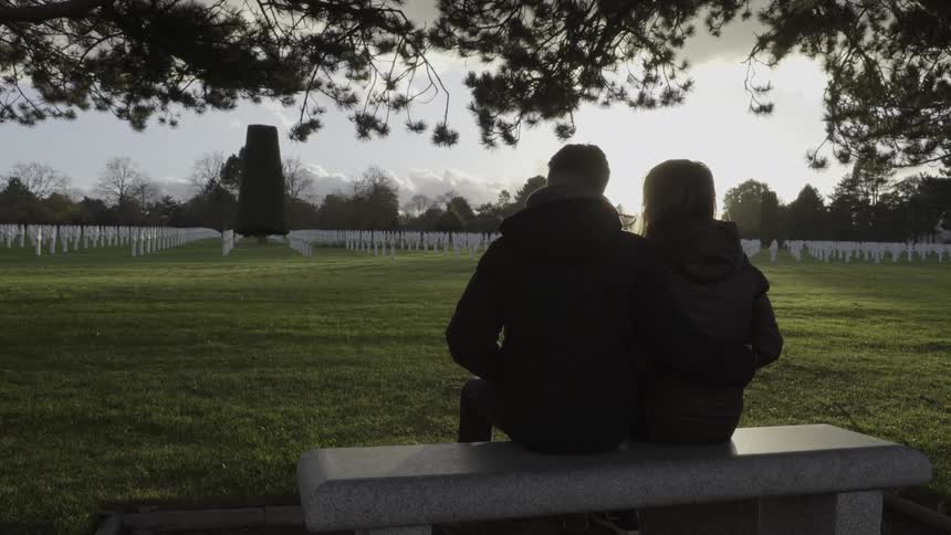 Two people sit on a bench looking over a cemetery