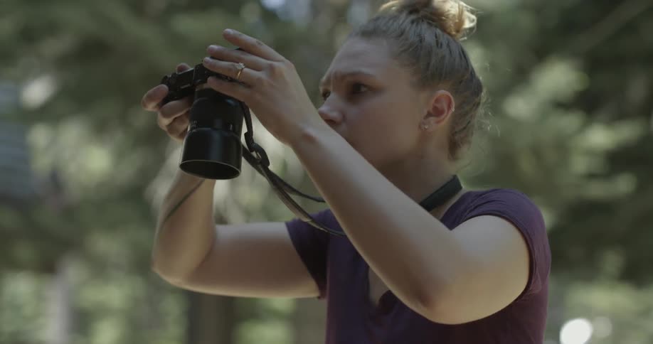 A woman adjusts her camera and takes pictures outside