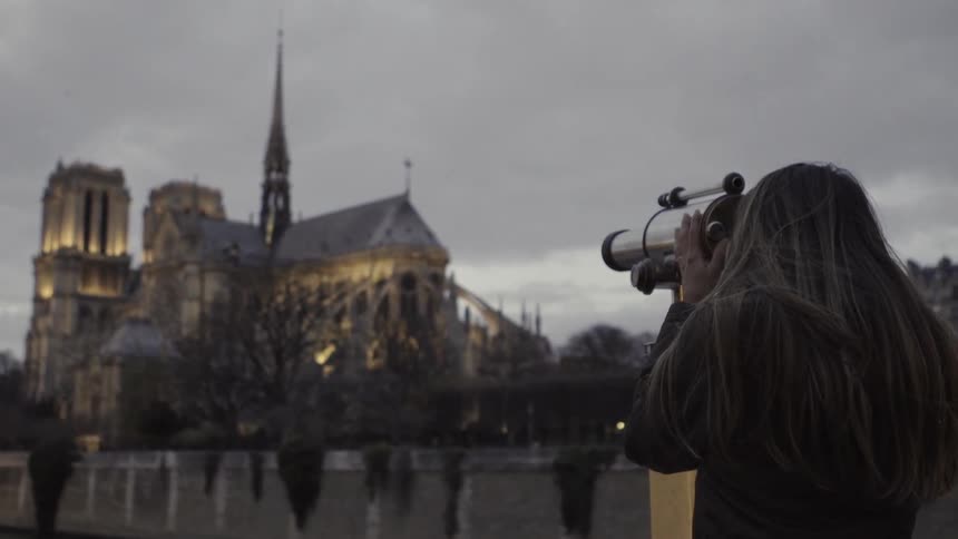 A woman is using a telescope to look at a view of a building