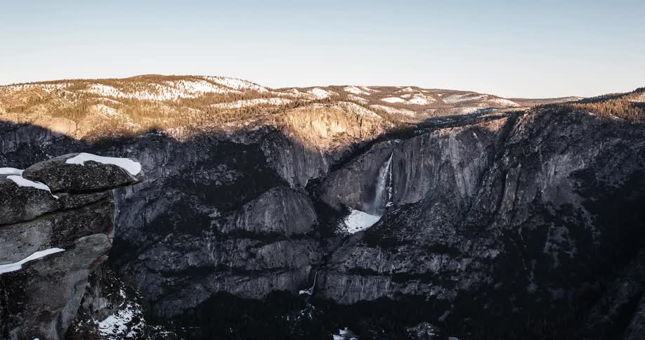 Clouds cast shadows a mountainside and waterfall