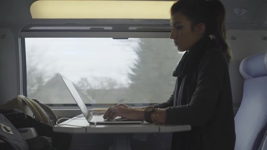 A woman types on a laptop while riding a train