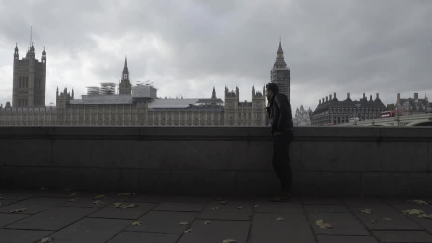 A man leans against a stone wall overlooking a city