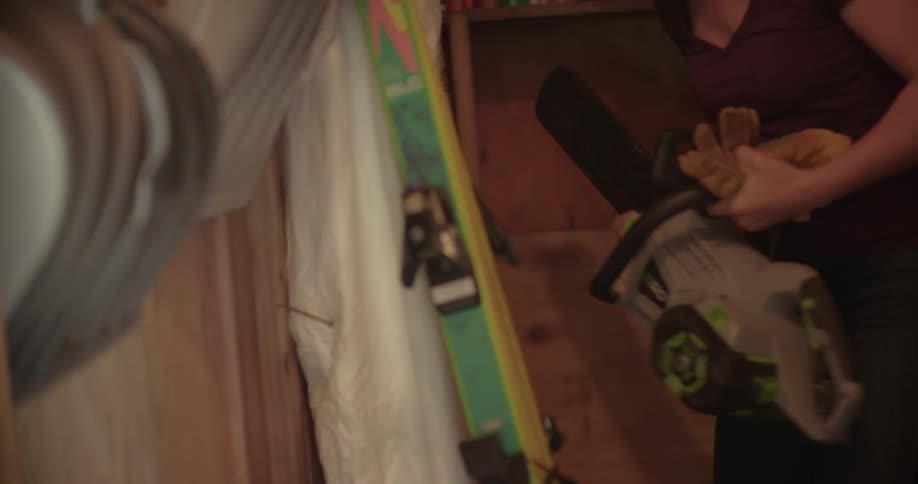 A woman brings a chainsaw out of her shed
