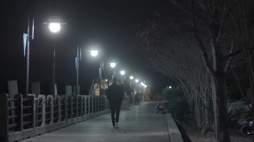 A man walks along a boardwalk alone at night