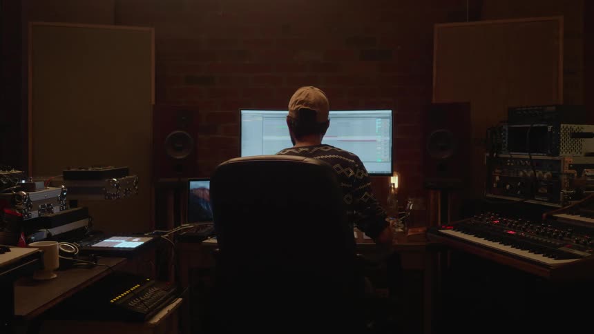 A man sits at a computer in a music studio
