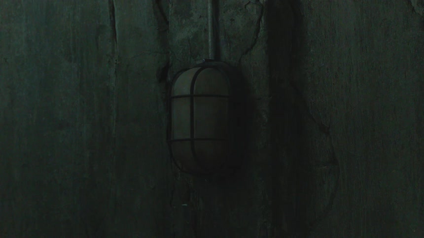 An ominous industrial cage light flickers on a dark, cracked concrete wall in a spooky basement