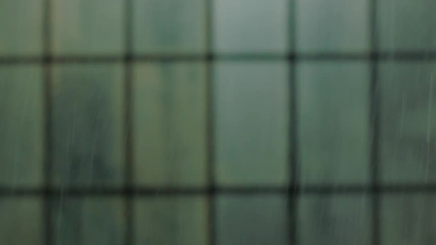 Rain falling heavily against a blurry window with a grid pattern