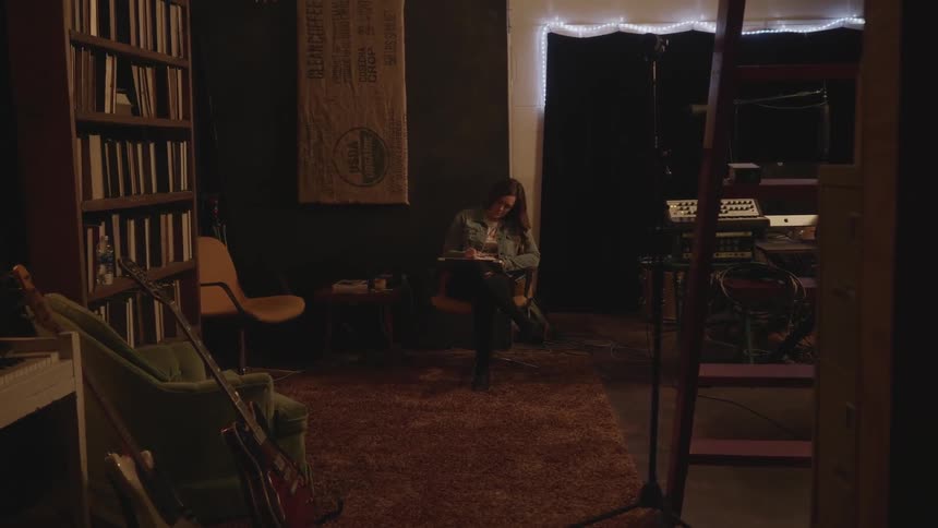 A woman sits in a dimly lit room with shelves of books