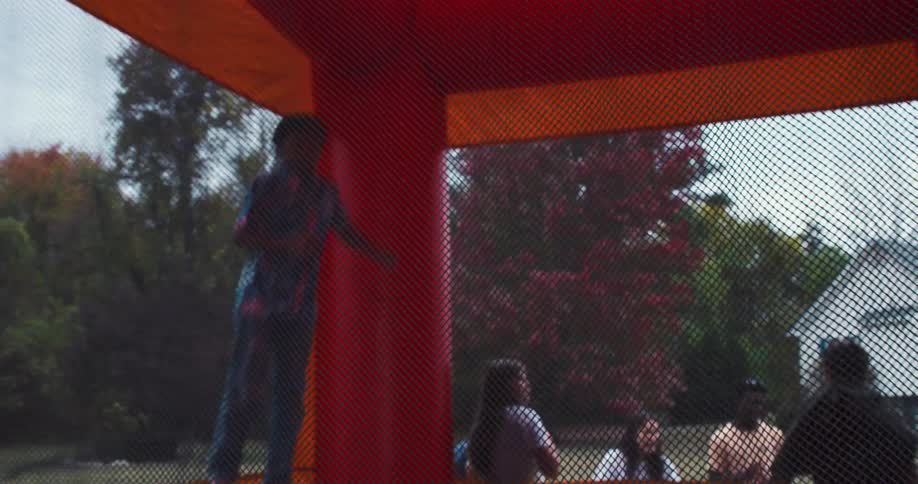 Slow motion shot of a boy doing a backflip in a bounce house as friends watch from the backyard