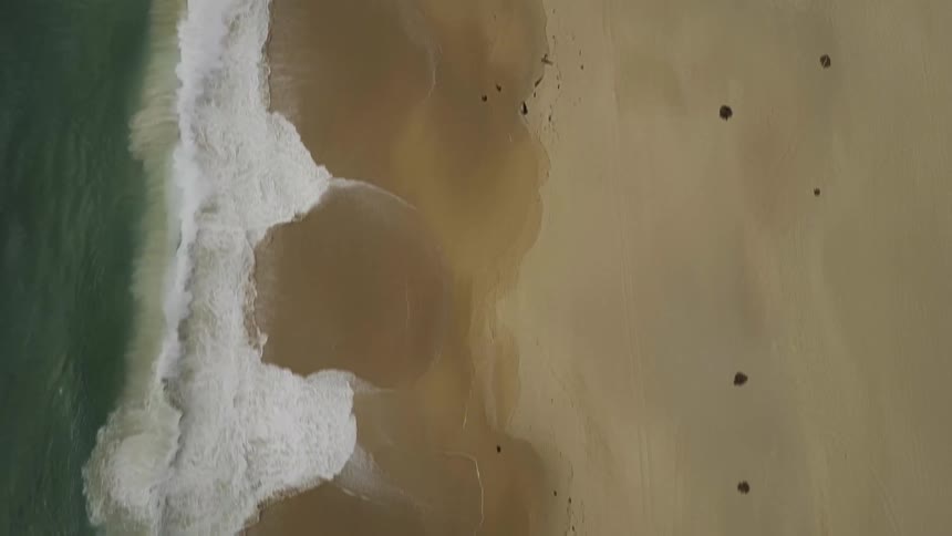 Aerial view of water coming ashore on a beach