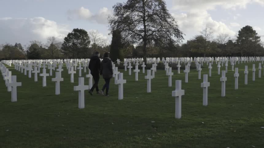 Two people pass tombstones in a cemetery