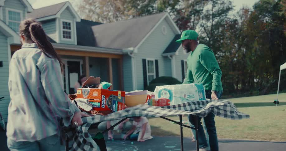 A woman and a man carry a food table in slow motion as neighbors and children gather for a block party
