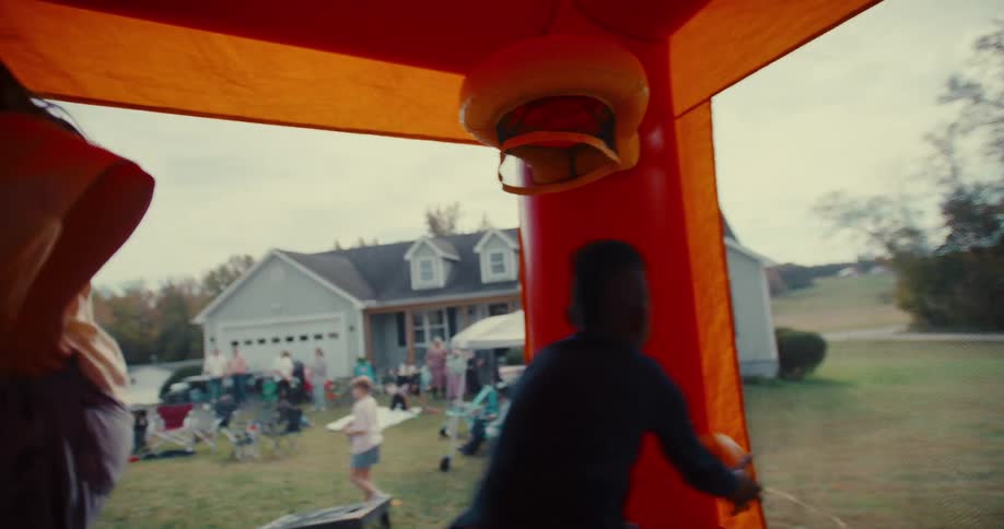 A young boy dunks a ball in slow motion while jumping in a bounce house with friends at a backyard party