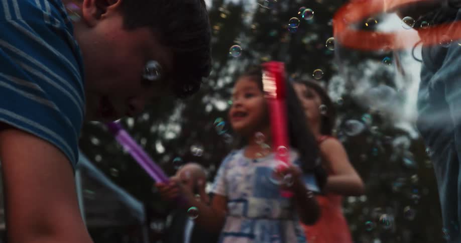 A group of diverse children laugh and play together, surrounded by a magical cloud of soap bubbles in slow motion