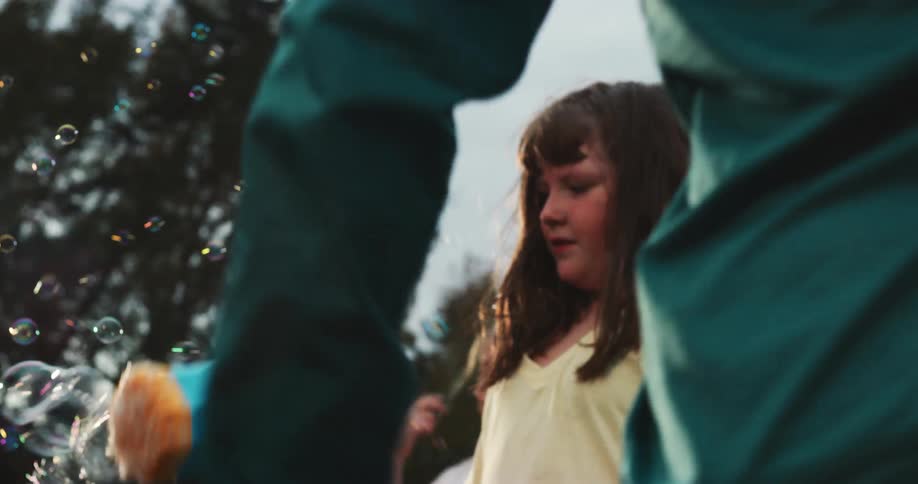 In slow motion, a group of kids joyfully play outside with a colorful bubble gun, surrounded by a stream of iridescent bubbles