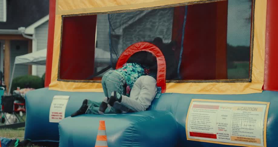 Two young boys in slow motion excitedly climb into a colorful bounce house at a backyard party