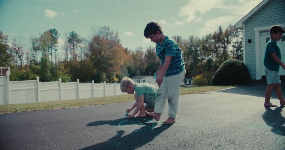 Three young friends laugh and play together while drawing with chalk on a suburban driveway on a sunny day