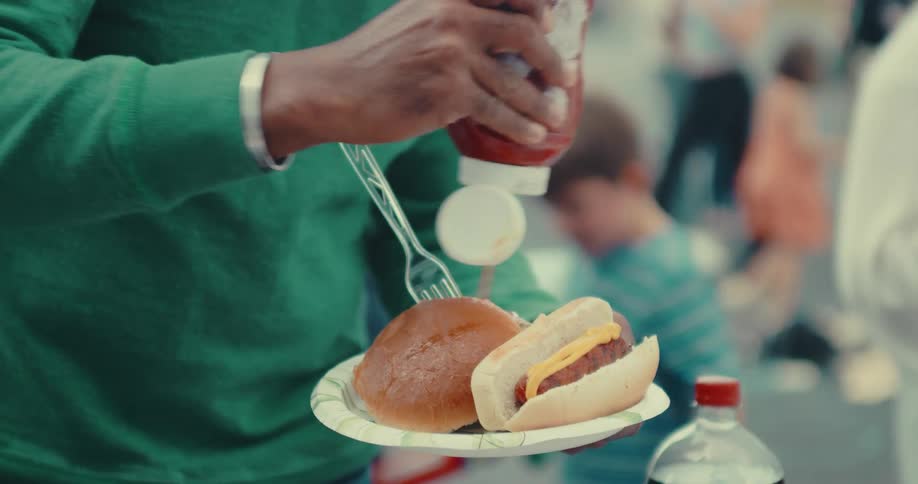 Close-up of a person putting ketchup on their food at a neighborhood barbecue party