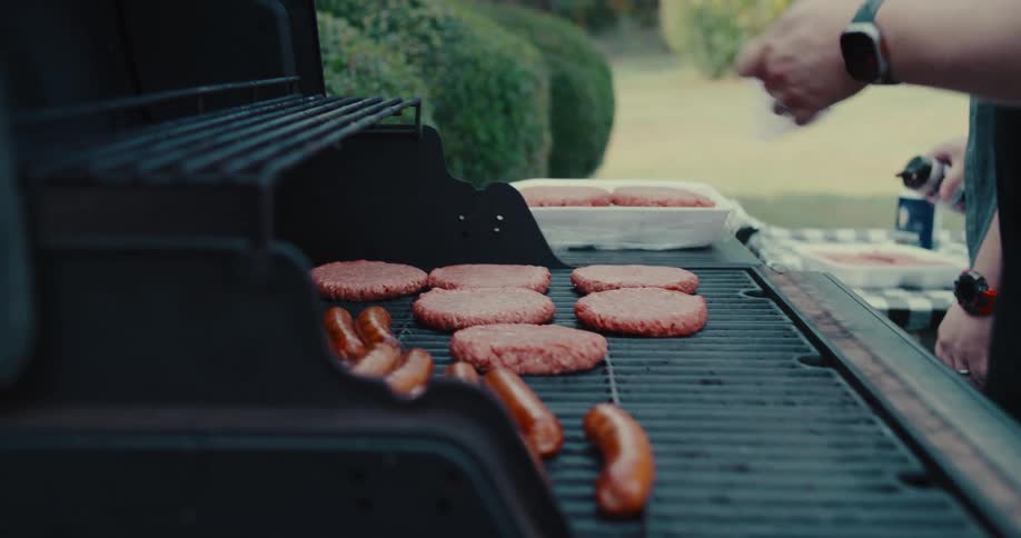 Close-up slow motion shot of a hand placing a raw hamburger patty on a hot grill for a backyard barbecue