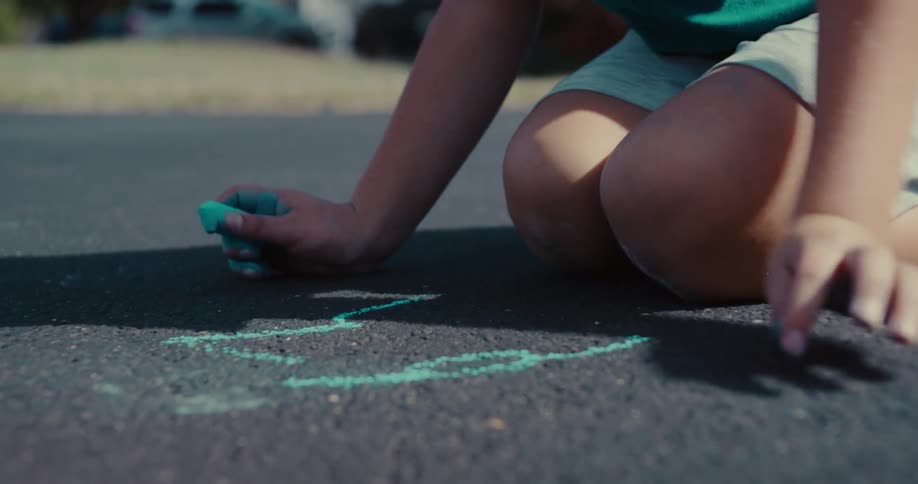 Slow motion close-up of a child's hand drawing a green chalk design on the asphalt