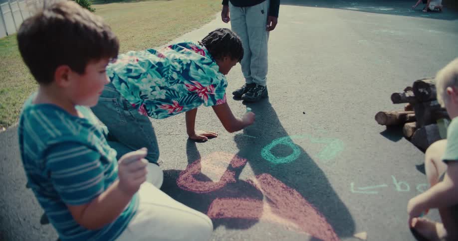 A diverse group of young boys play together, drawing colorful pictures with chalk on the pavement on a sunny day
