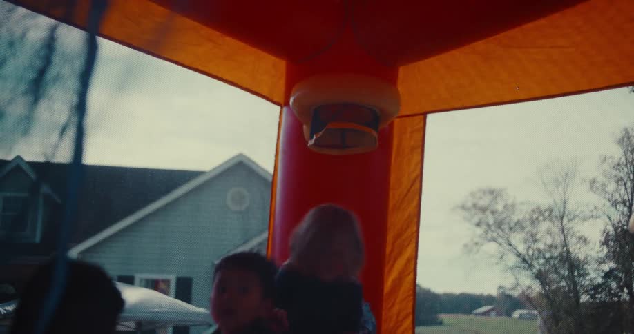 Silhouetted children joyfully jump and play basketball inside a colorful bounce house in slow motion