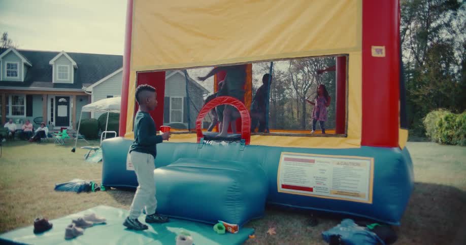 Children joyfully jump and play in a large bounce house in slow motion during a backyard party