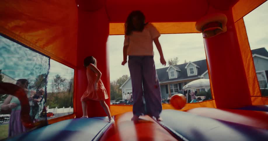 Slow motion footage from inside a colorful bounce house shows happy children jumping and playing at a backyard party