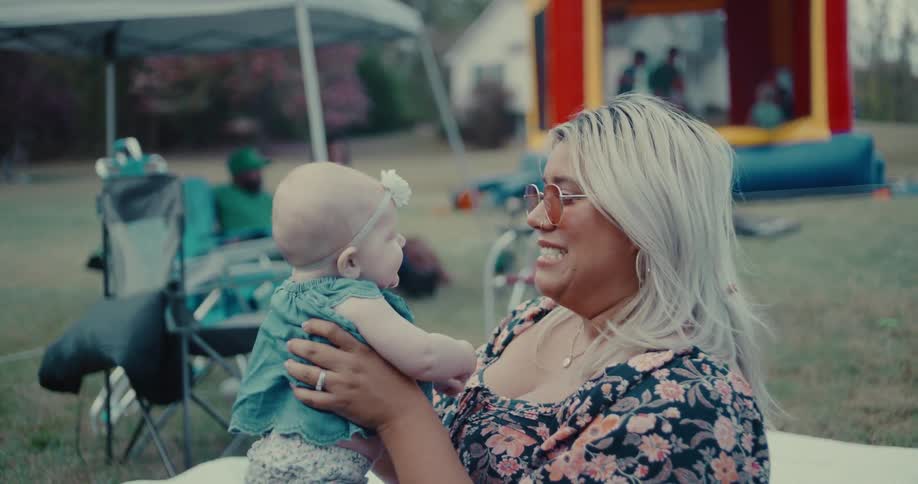 A smiling mother holds her baby girl and laughs during a fun outdoor party in slow motion