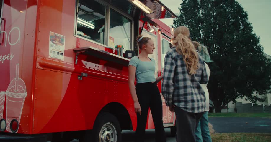 Three teenage girls laugh and talk together while waiting to order from a red food truck in the evening