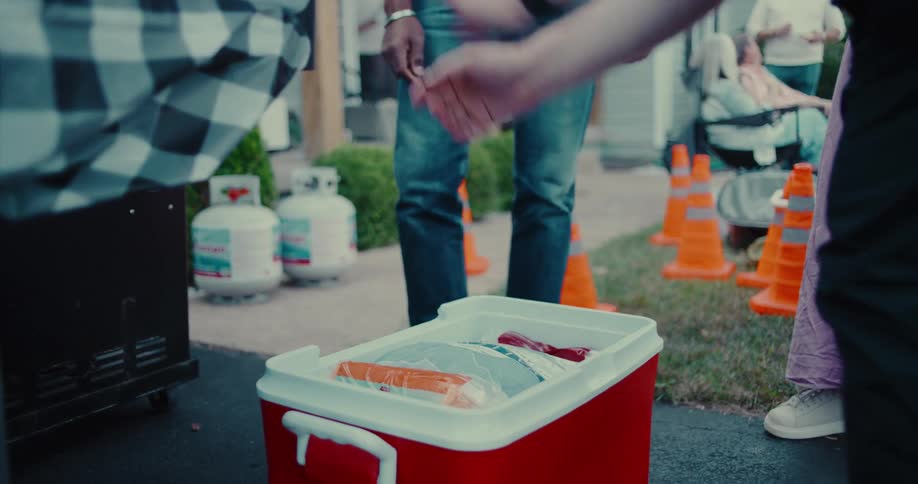 A person places packaged food items into a red cooler filled with ice at a neighborhood gathering