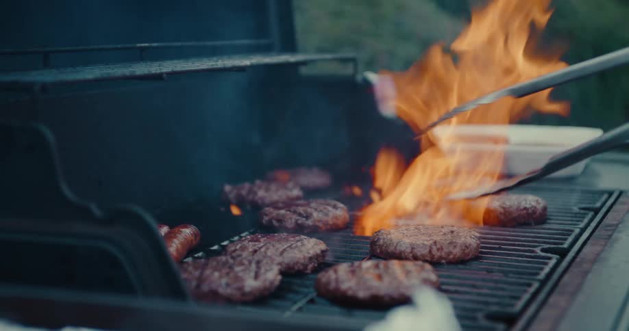 Close-up shot of juicy hamburgers cooking on a flaming barbecue grill in slow motion