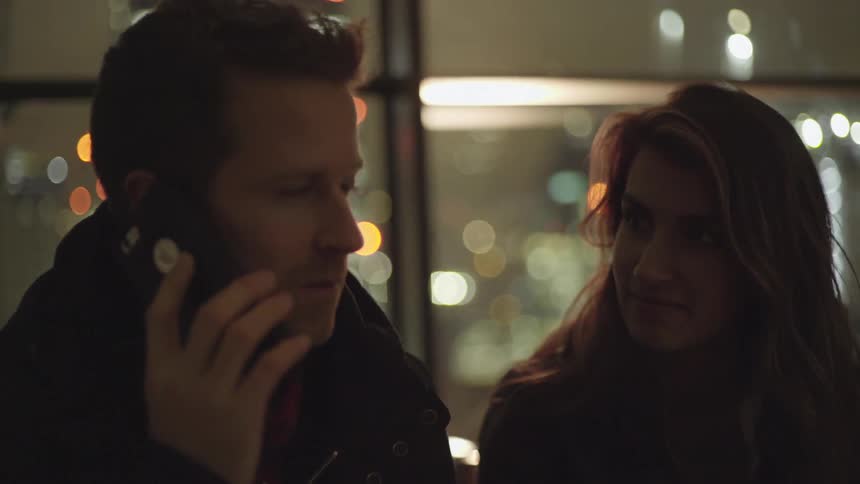 A man answers his cell phone sitting next to a woman