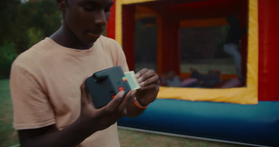 A young man takes an instant photograph at an outdoor event and shakes the print to develop it