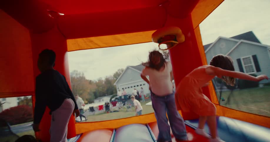 A group of diverse children joyfully jump and play inside a colorful bounce house in slow motion during an outdoor party