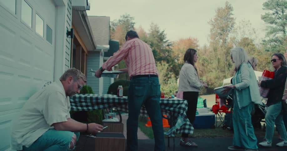 Neighbors and friends gather in a driveway for a community block party, bringing dishes to share at a potluck table