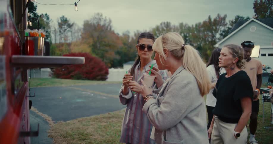 A group of friends enjoys drinks and conversation while waiting in line at an outdoor food truck